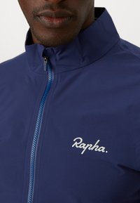 Navyfarbene Fahrradjacke mit hohem Kragen, Frontreißverschluss und reflektierendem Logo. Glatte Textur, leichtes Material, ideal für Outdoor-Aktivitäten.