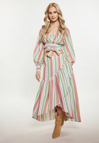 Abito lungo a righe multicolori con orlo arricciato, cintura in vita e maniche lunghe e voluminose. Indossato con stivali da cowboy beige.