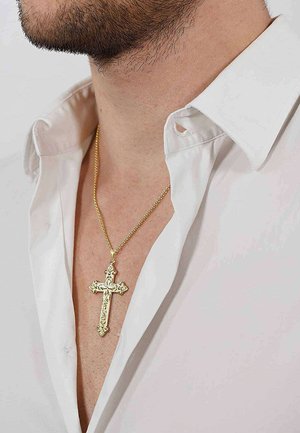 Mann trägt ein weißes Hemd mit offenem Kragen und eine detaillierte goldene Kreuzanhänger-Halskette um den Hals.