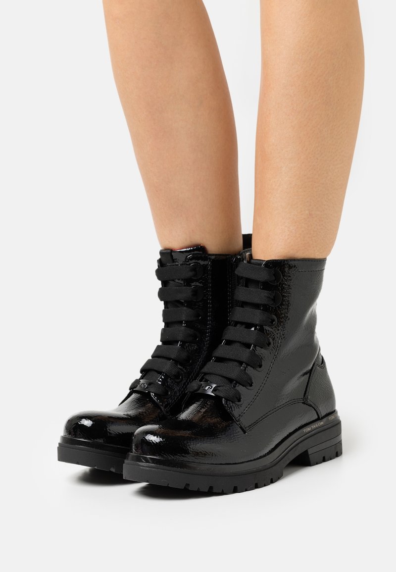Bottes courtes en cuir verni noir avec bouts ronds, surface texturée, devant à lacets, talon renforcé et semelles en caoutchouc antidérapantes.