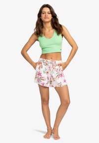 Groene geribbelde crop top met een ronde halslijn, gecombineerd met witte bloemen short met roze en groene patronen en een elastische tailleband.
