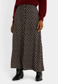 Jupe midi fluide noire avec un motif floral ivoire, dotée de boutons sur le devant, d'une taille haute et d'une texture douce. Portée avec des bottines noires.