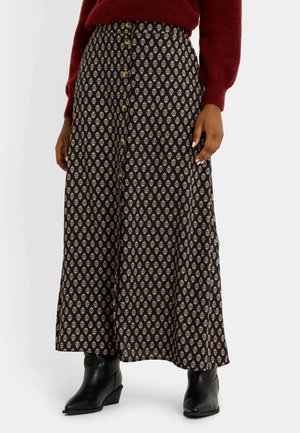 Jupe midi fluide noire avec un motif floral ivoire, dotée de boutons sur le devant, d'une taille haute et d'une texture douce. Portée avec des bottines noires.