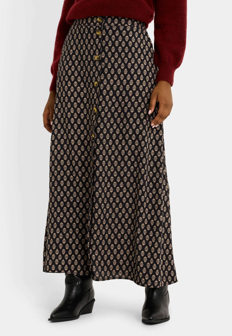 Jupe midi fluide noire avec un motif floral ivoire, dotée de boutons sur le devant, d'une taille haute et d'une texture douce. Portée avec des bottines noires.
