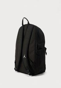 Μαύρο σακίδιο πλάτης με ανθεκτικό ύφασμα, ενισχυμένους ιμάντες ώμων, πλαϊνές θήκες και λευκό λογότυπο Jumpman στο μπροστινό μέρος.