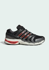 Baskets de sport noires et rouges avec semelle blanche, dessus en mesh et grip texturé, montrées en profil latéral sur un fond clair.