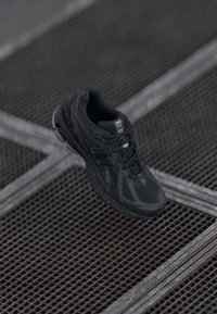 Botte de sport noire avec une tige en mesh, des accents texturés et une semelle rembourrée. Design à lacets et détail de logo sur le côté.