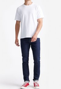 Witte katoenen T-shirt met korte mouwen, gecombineerd met donkerblauwe denim jeans en rode sneakers. Eenvoudig ontwerp zonder zichtbare patronen of logo's.