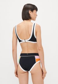 Czarny biustonosz bikini z szerokimi ramiączkami i białym wykończeniem, z zapięciem na klamrę. Wysokie majtki z kolorowymi panelami w geometryczne wzory po bokach.