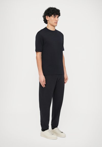 Fekete rövid ujjú póló sötét nadrággal párosítva, laza szabással és sima textúrával, világos színű tornacipővel kiegészítve.