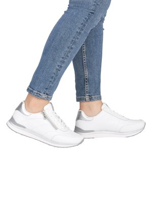 Weiße Sneaker mit silbernen Akzenten, strukturiertem Leder und einem seitlichen Reißverschluss. Kombiniert mit blauen Jeans, die ein sportliches Design und eine leichte Sohle zeigen.
