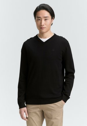 Schwarzer V-Ausschnitt-Pullover aus weichem Strickstoff, mit enganliegendem Design und gerippten Bündchen und Saum, kombiniert mit beigen Hosen.