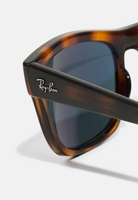 Ochelari de soare tortoise brown cu lentile întunecate, având un design elegant și un logo metalic Ray-Ban pe lateral pentru branding.