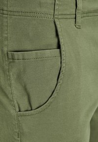 Pantaloni in cotone verde con tasca laterale, cuciture a vista e una texture di tessuto liscia. Design minimalista con taglio dritto.