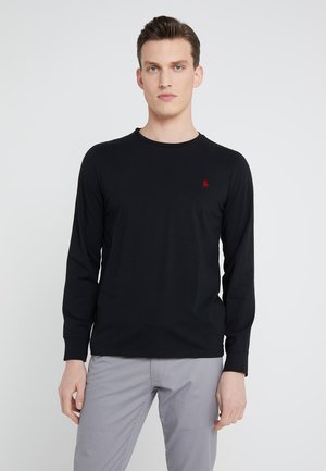 Black long-sleeve shirt in soft cotton, featuring a round neckline and a small red logo on the chest. Paired with light gray trousers.