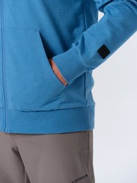 Felpa blu chiaro con zip, caratterizzata da un tessuto strutturato, tasche laterali e polsini a coste. Abbinata a pantaloni corti grigi con un dettaglio del logo sulla gamba.