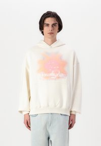 Hellbeige übergroße Kapuzenjacke mit einem rosa und blauen Sonnenmotiv auf der Vorderseite. Mit einer Kängurutasche und verstellbarem Kordelzug in der Kapuze gestaltet.