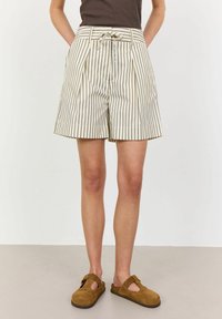 Striped shorts with a high waist, pleats, and a tie belt in cream and dark brown. Worn with brown suede slip-on shoes.