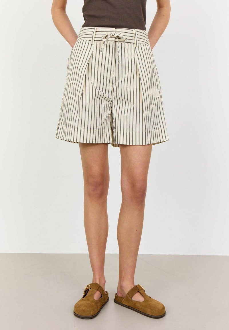 Shorts rayés taille haute avec des plis et une ceinture à nouer en crème et marron foncé. Portés avec des chaussures slip-on en daim marron.