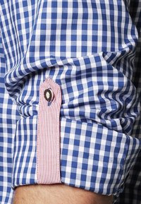 Blauw en wit geruite mouw van een overhemd met een roze en wit gestreepte binnenvoering, voorzien van een decoratieve knop op de flap.