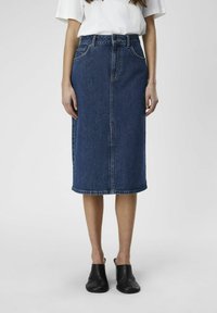 Denim midi-skjørt i blått med rett snitt, frontlukk med knapper, beltehemper og hemmede kanter; brukt med svarte slip-on-sko.
