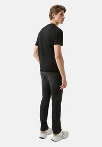 Sort strikket t-shirt med korte ærmer, kombineret med mørke jeans og hvide sportssko. Modellen vist bagfra. Simpelt design uden mønstre.