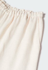 Tissu rose clair à texture douce, avec une ceinture élastique et une coupe ample. Comprend des poches latérales pour plus de fonctionnalité.