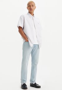 Camisa de botones de manga corta con rayas blancas y en tonos pastel, combinada con jeans azul claro y mocasines negros, presentando un corte relajado y una textura suave.