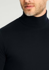 Canottiera nera a collo alto realizzata in tessuto a coste, con un design aderente e un colletto alto, che mette in mostra una texture liscia e uno stile minimalista.
