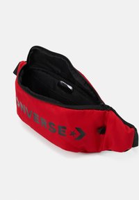 Czerwony nerka z czarnym zamkiem i wnętrzem, z logo "Converse" w czerni na przodzie. Kompaktowy i lekki design.