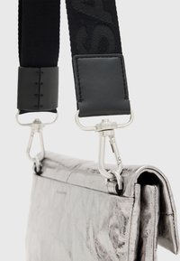 Borsa in pelle metallizzata argento con finitura testurizzata, dotata di una tracolla in tessuto nero con motivo a logo e attacchi per fibbia in metallo argentato.