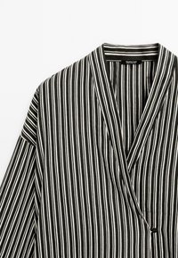 Black and white striped wrap shirt. Lightweight fabric, features a shawl collar, long sleeves, and a single button detail near the hem.