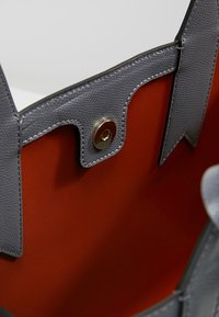 Szara skórzana torba na ramię z pomarańczowym wnętrzem, z złotym zapięciem na zatrzask i dekoracyjnymi skórzanymi akcentami.