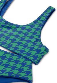 Plivanje set s plavom podlogom i zelenim uzorkom zvijezda, s sportskim krojem i rastezljivom tkaninom. Detalji šavova oko rubova su vidljivi.