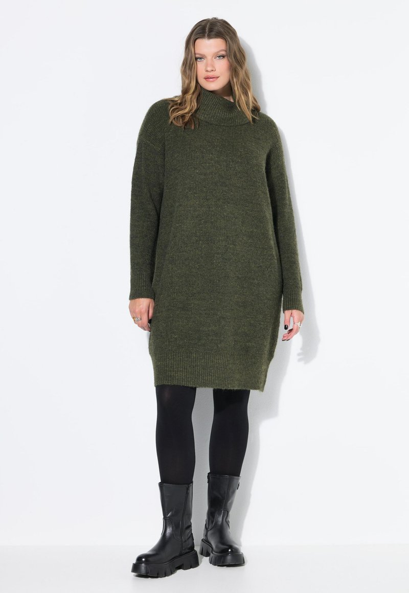 Abito lungo verde a collo alto oversize in maglia, con maniche lunghe, fessure laterali e bordo a costine, abbinato a stivali neri corposi. Texture liscia, design casual.