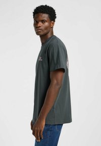 Szara bawełniana koszulka z krótkim rękawem, z okrągłym dekoltem. Posiada różowy nadruk na piersi oraz logo na plecach. Regularny krój, gładka tekstura.