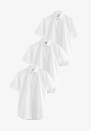 Trijų baltų trumpomis rankovėmis marškinių ekspozicija. Kiekvienas marškinys turi klasikinį apykaklę, sagčių užsegimą ir glotnų, lengvą audinio tekstūrą.