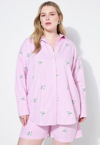 Camicia oversize a righe rosa chiaro con ricami floreali e chiusura a bottoni, abbinata a pantaloni corti coordinati, che mostra una vestibilità rilassata.