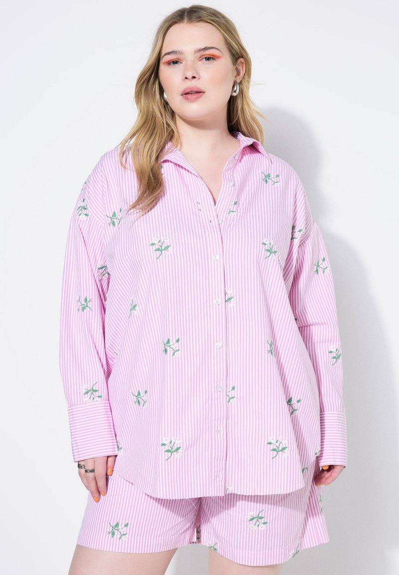 Camicia oversize a righe rosa chiaro con ricami floreali e chiusura a bottoni, abbinata a pantaloni corti coordinati, che mostra una vestibilità rilassata.