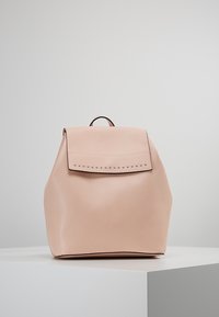 Reppu pehmeästä vaaleanpunaisesta nahasta, jossa on jäsennelty muotoilu, tasainen yläkansi ja metalliset niitit reunan ympärillä. Varustettu yläkahvalla kantamista varten.