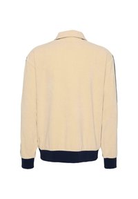 Beżowa bluza z kołnierzem, granatowymi prążkowanymi mankietami i dołem, o miękkiej fakturze. Gładkie plecy bez dodatkowych wzorów i elementów metalowych.