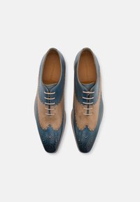 Scarpe in pelle bicolore con parte superiore color cuoio e punta blu scuro, caratterizzate da dettagli perforati e stringhe a contrasto. Design a punta. 