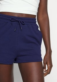 Shorts en mélange de coton bleu marine avec taille élastique, fermeture par cordon de serrage et poches latérales, affichant une texture lisse et une coupe décontractée.