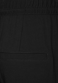 Zwarte stoffen broek met een gladde textuur, voorzien van een geplooide tailleband en een platte achterzak met contrasterende stiksels.