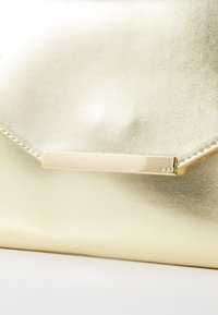 Aranyfémes clutch táska sima textúrával, szögletes dizájnnal és lapos arany hardver díszítéssel az elején.