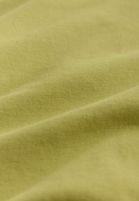 Gros plan sur un tissu tricoté doux vert clair montrant une fine texture côtelée et de légers plis.