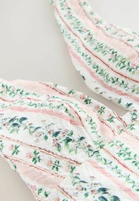 Gros plan sur un tissu de maillot de bain rose et blanc avec des motifs floraux verts et roses et des détails de couture texturée.