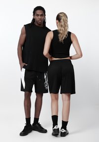 Top preto sem mangas e calções com padrão de chamas brancas. O modelo masculino usa ténis pretos, enquanto a modelo feminina usa meias e sapatos pretos.