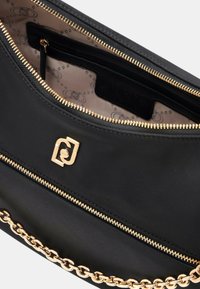 Clutch bag in tessuto nero con una tracolla in catena dorata, chiusura a zip dorata, e un interior liscio con etichetta del marchio e tasca con zip.