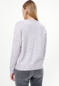 Strukturierter hellgrauer Pullover mit rosa und blauen Sprenkeln, runder Ausschnitt, überschnittene Schultern und gerippter Saum. Getragen mit dunkelgrauen Jeans.
